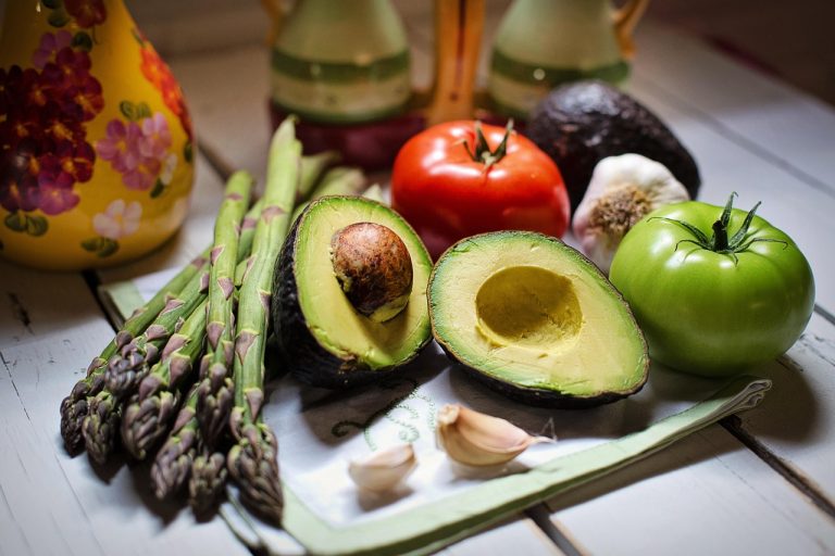 Fresh vegetables and avocado on a table with asparagus, tomato, and garlic.