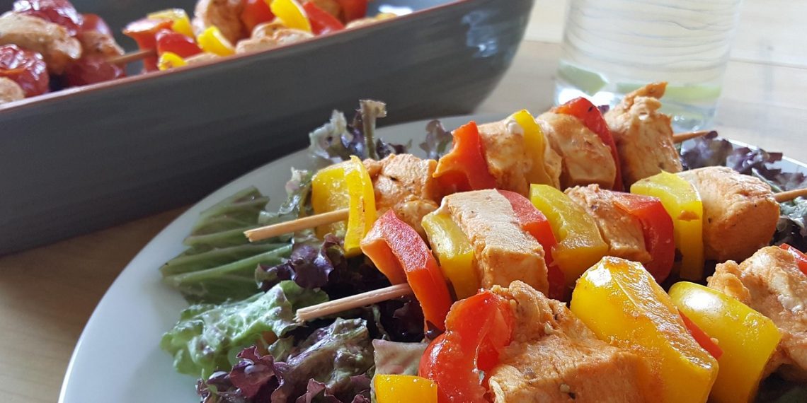 Grilled chicken skewers with bell peppers on a bed of fresh lettuce.