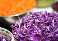 Shredded purple cabbage in a bowl surrounded by sliced vegetables.