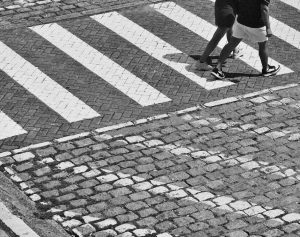 Pedestrians crossing a cobblestone street at a zebra crossing.