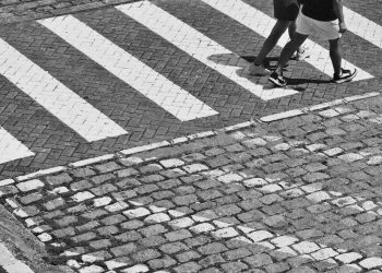Pedestrians crossing a cobblestone street at a zebra crossing.
