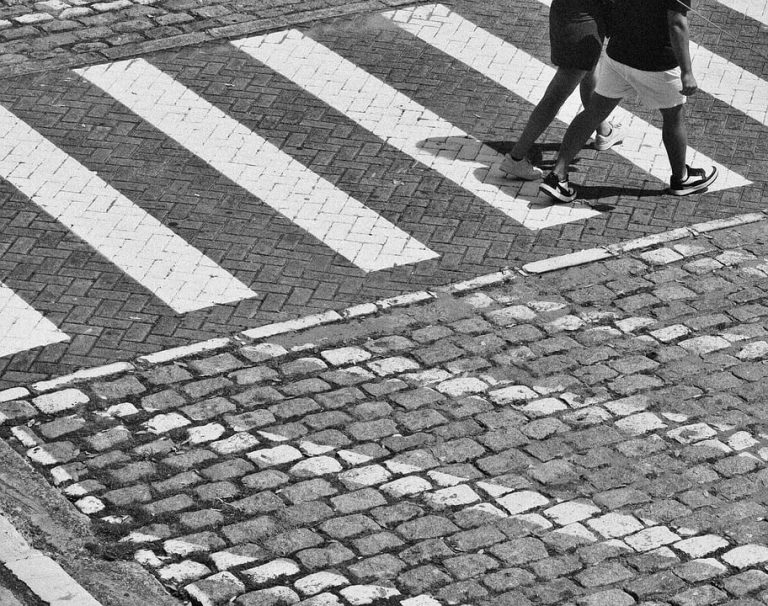 Pedestrians crossing a cobblestone street at a zebra crossing.
