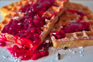 Waffles topped with vibrant berry sauce and powdered sugar.