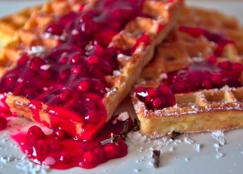 Waffles topped with vibrant berry sauce and powdered sugar.