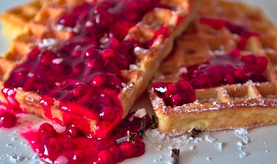 Waffles topped with vibrant berry sauce and powdered sugar.