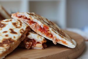 Grilled quesadillas with melted cheese and tomato filling on a wooden board.