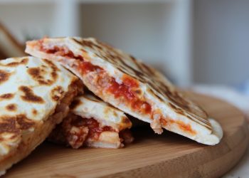 Grilled quesadillas with melted cheese and tomato filling on a wooden board.