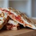 Grilled quesadillas with melted cheese and tomato filling on a wooden board.