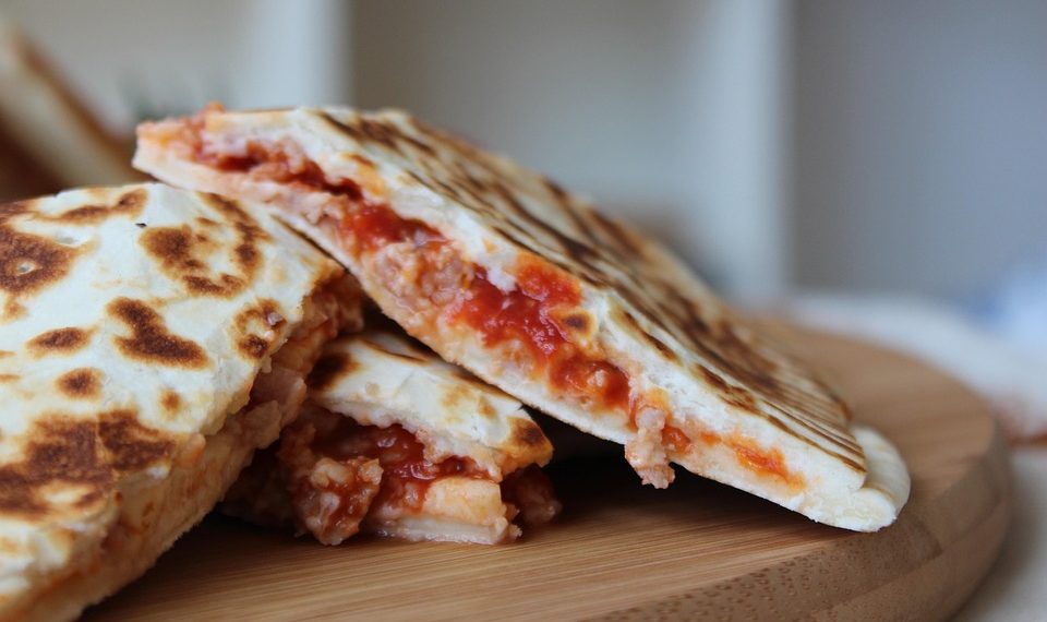 Grilled quesadillas with melted cheese and tomato filling on a wooden board.