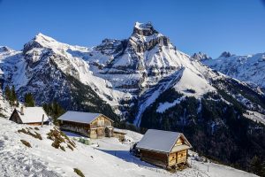 Snow-covered alpine cabins with majestic mountains in the background.