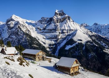 Snow-covered alpine cabins with majestic mountains in the background.