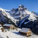 Snow-covered alpine cabins with majestic mountains in the background.