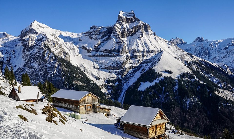 Snow-covered alpine cabins with majestic mountains in the background.