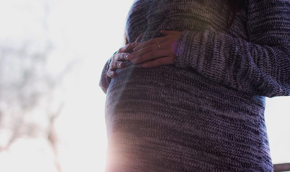 Pregnant woman cradling belly in cozy sweater.