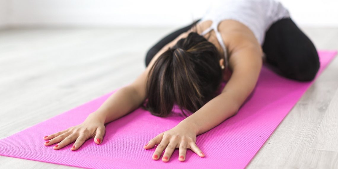 Woman practicing yoga child's pose on a pink mat.