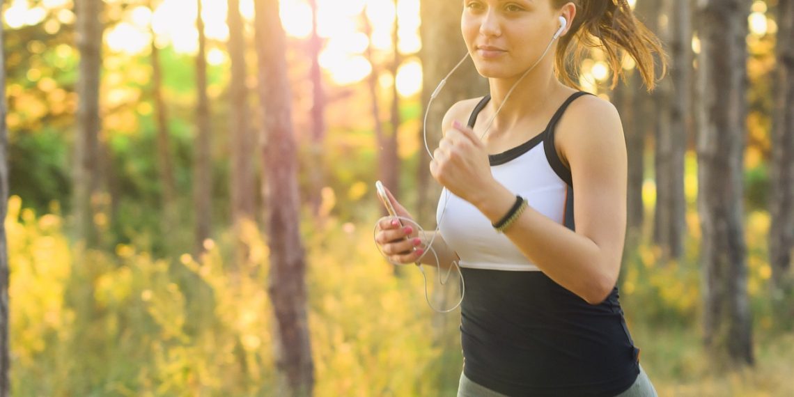 Woman jogging with headphones in a sunlit forest.