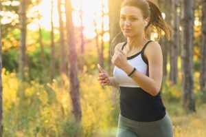 Woman jogging with headphones in a sunlit forest.