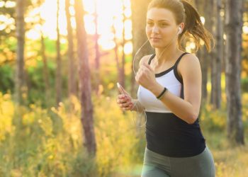 Woman jogging with headphones in a sunlit forest.