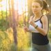 Woman jogging with headphones in a sunlit forest.