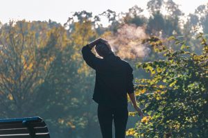 Person standing near bench in park, exhaling on a chilly morning.