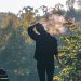 Person standing near bench in park, exhaling on a chilly morning.