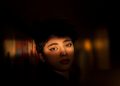 Shadowed face with intense gaze against a textured wall.