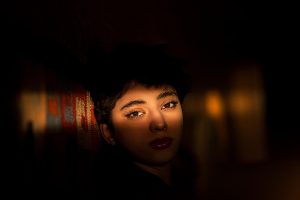 Shadowed face with intense gaze against a textured wall.