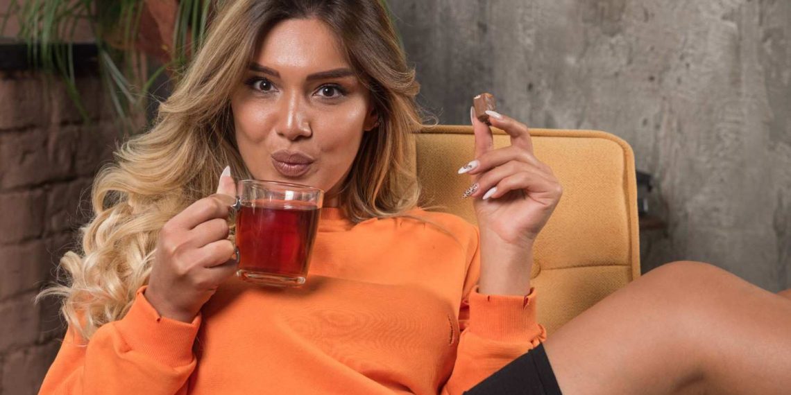 Woman enjoying tea and chocolate while relaxing on a chair.