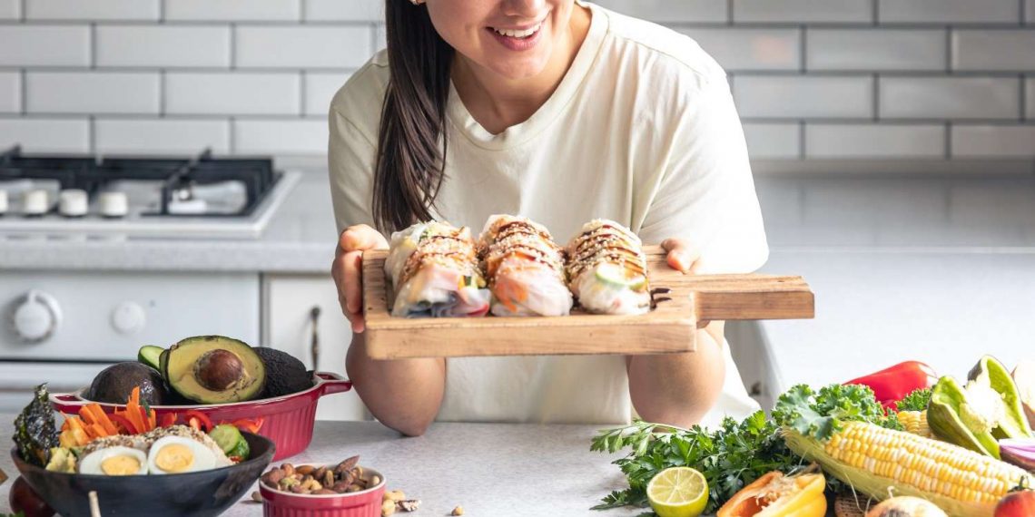 Woman holding fresh sushi rolls with vegetables on a kitchen counter.
