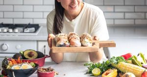 Woman holding fresh sushi rolls with vegetables on a kitchen counter.