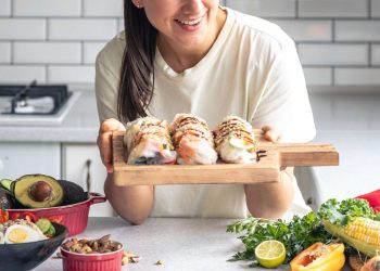Woman holding fresh sushi rolls with vegetables on a kitchen counter.