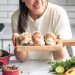 Woman holding fresh sushi rolls with vegetables on a kitchen counter.
