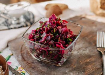 Beet salad with herbs in a glass bowl on wooden table.