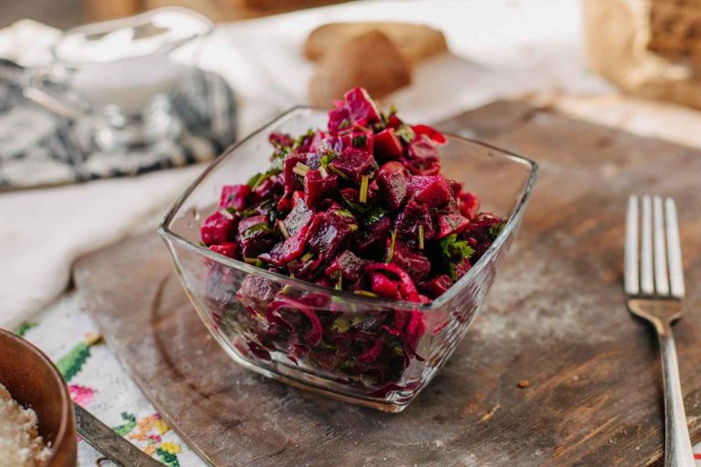 Beet salad with herbs in a glass bowl on wooden table.