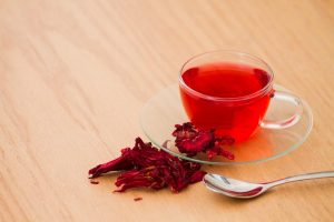 Glass cup of hibiscus tea with dried petals on wooden table.