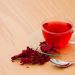 Glass cup of hibiscus tea with dried petals on wooden table.