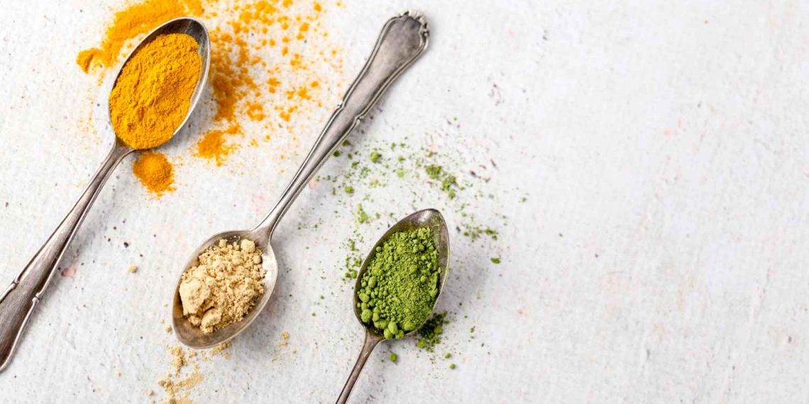 Spoons with turmeric, ginger, and matcha powder on a white background.