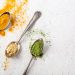 Spoons with turmeric, ginger, and matcha powder on a white background.