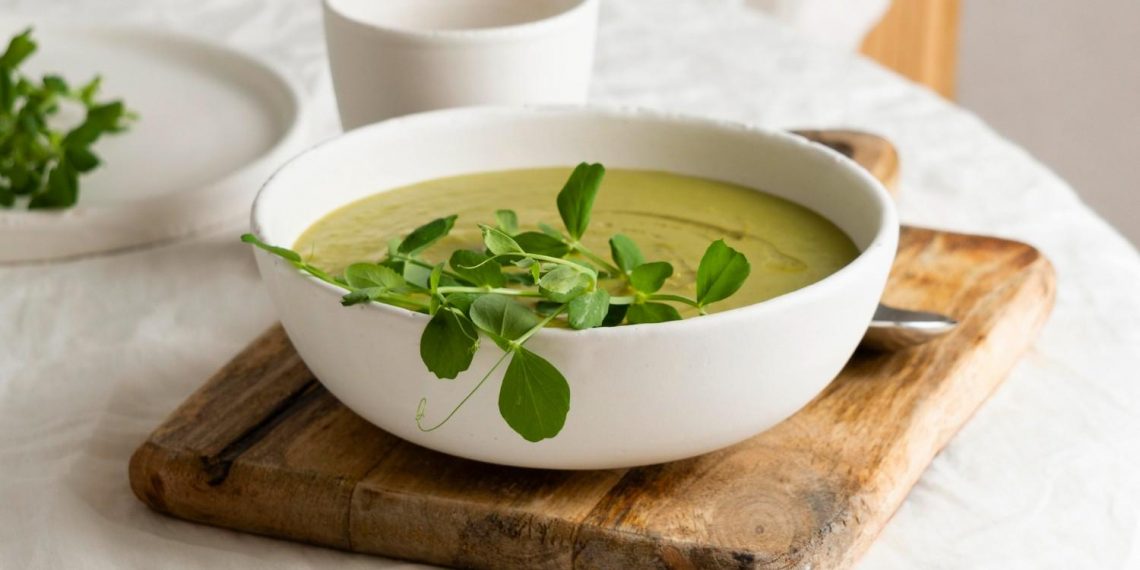 Creamy pea soup garnished with fresh greens on a wooden board.
