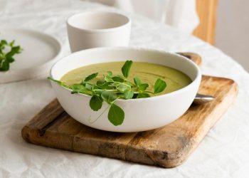 Creamy pea soup garnished with fresh greens on a wooden board.