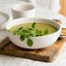 Creamy pea soup garnished with fresh greens on a wooden board.