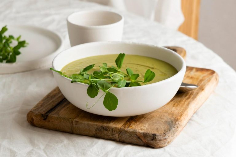 Creamy pea soup garnished with fresh greens on a wooden board.
