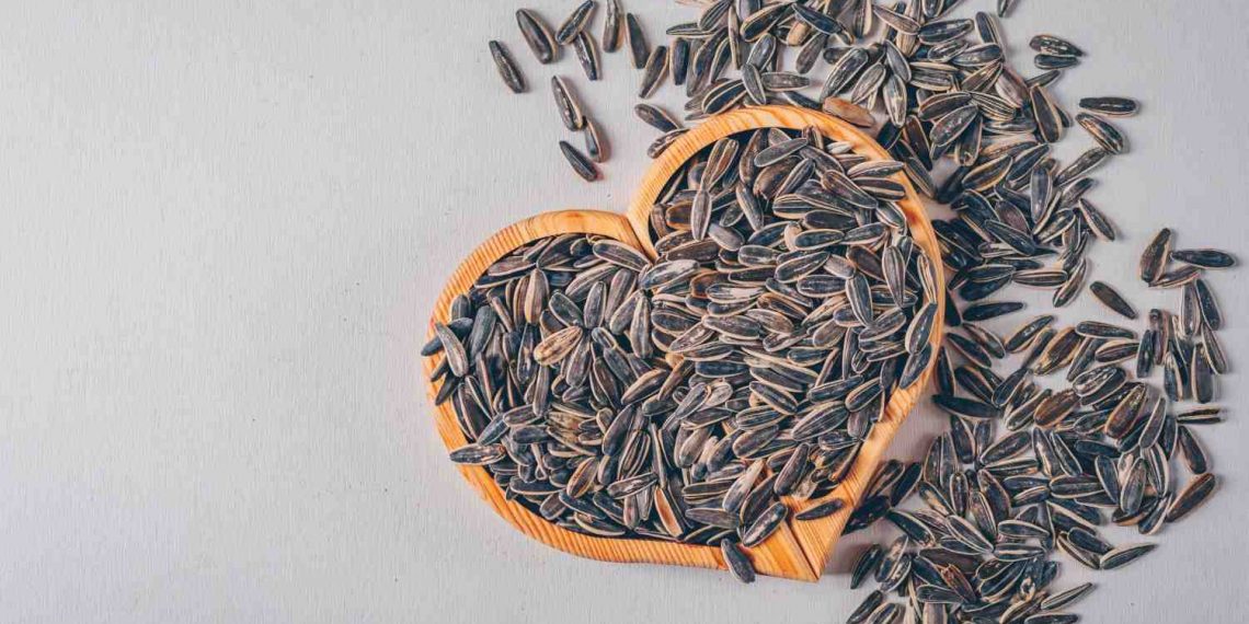 Sunflower seeds in a heart-shaped bowl scattered on a table.