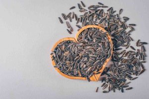 Sunflower seeds in a heart-shaped bowl scattered on a table.