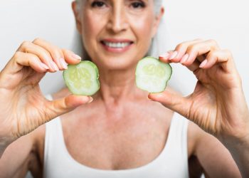 Senior woman smiling and holding cucumber slices.