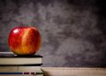 Apple resting on a stack of books against a chalkboard background.