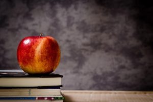 Apple resting on a stack of books against a chalkboard background.