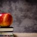 Apple resting on a stack of books against a chalkboard background.