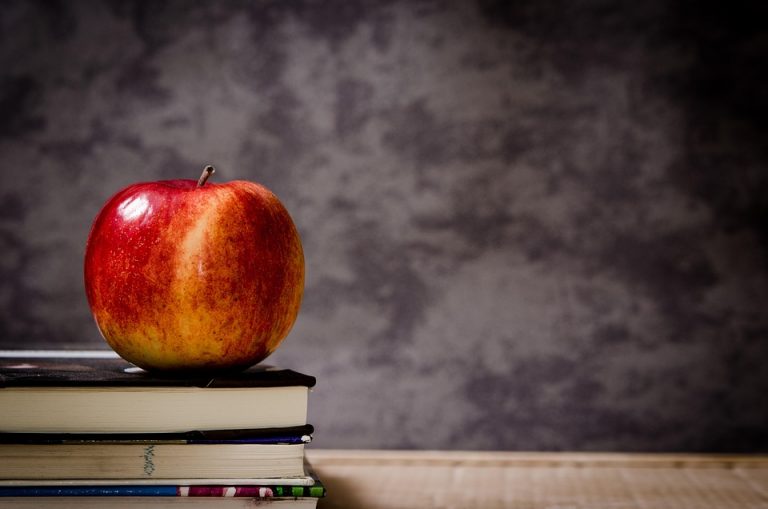 Apple resting on a stack of books against a chalkboard background.