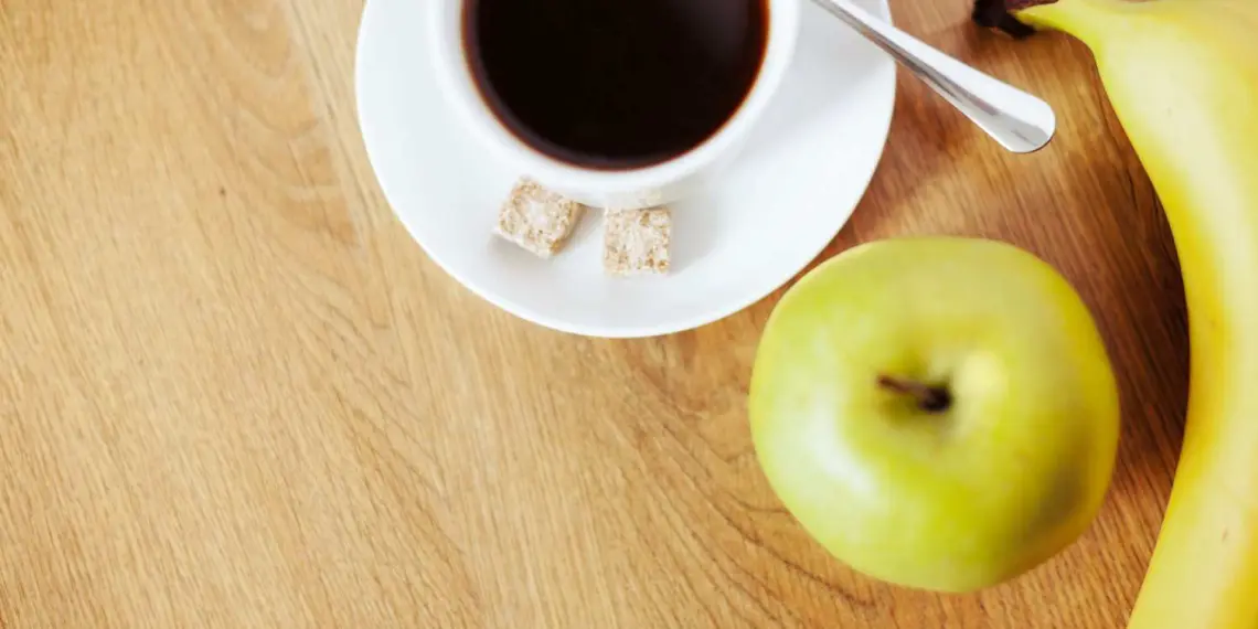 Cup of coffee with green apple and banana on wooden table.